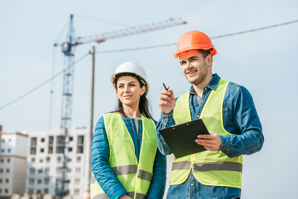 stock-photo-smiling-surveyor-clipboard-pointing-away-colleague-construction-site